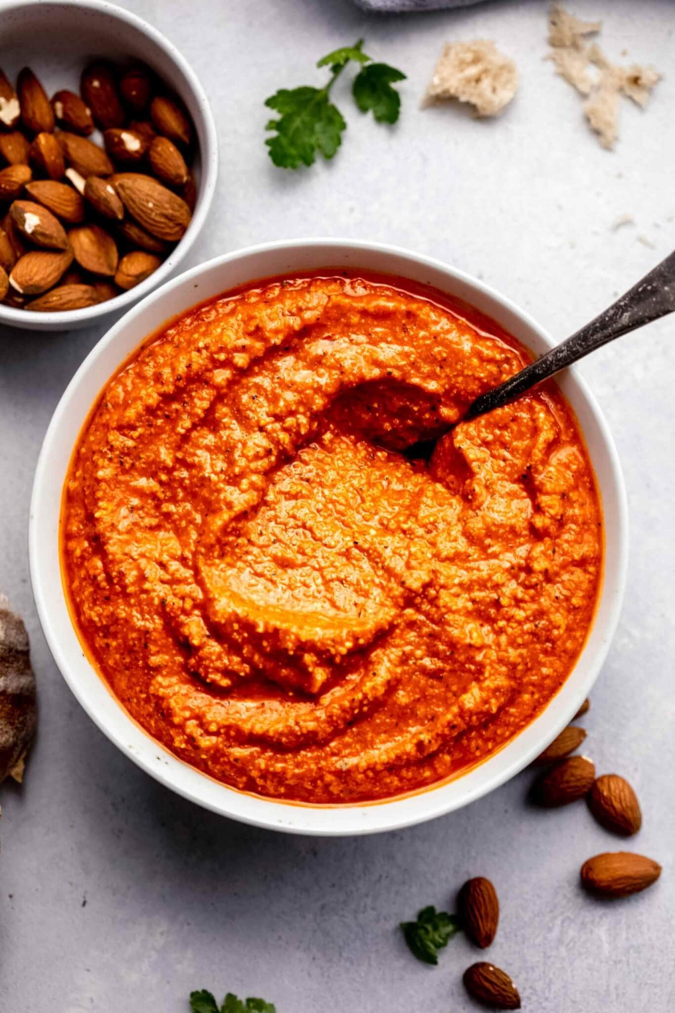 Romesco sauce in white bowl next to almonds and crusty bread.