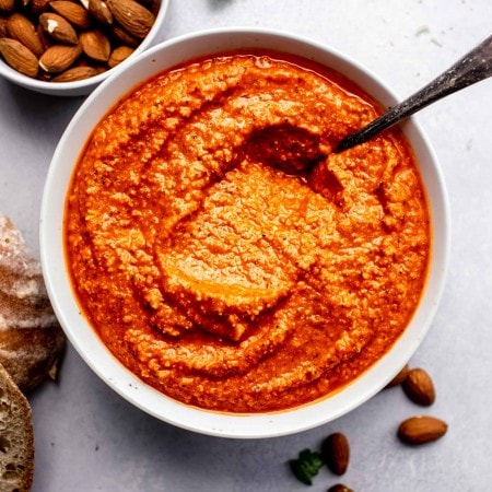 Romesco sauce in white bowl next to almonds and crusty bread.