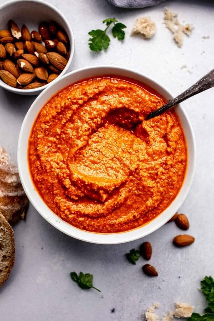 Romesco sauce in white bowl next to almonds and crusty bread.