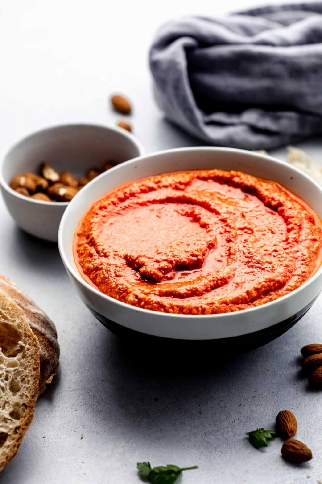 Side view of Romesco sauce in white bowl next to almonds and crusty bread.