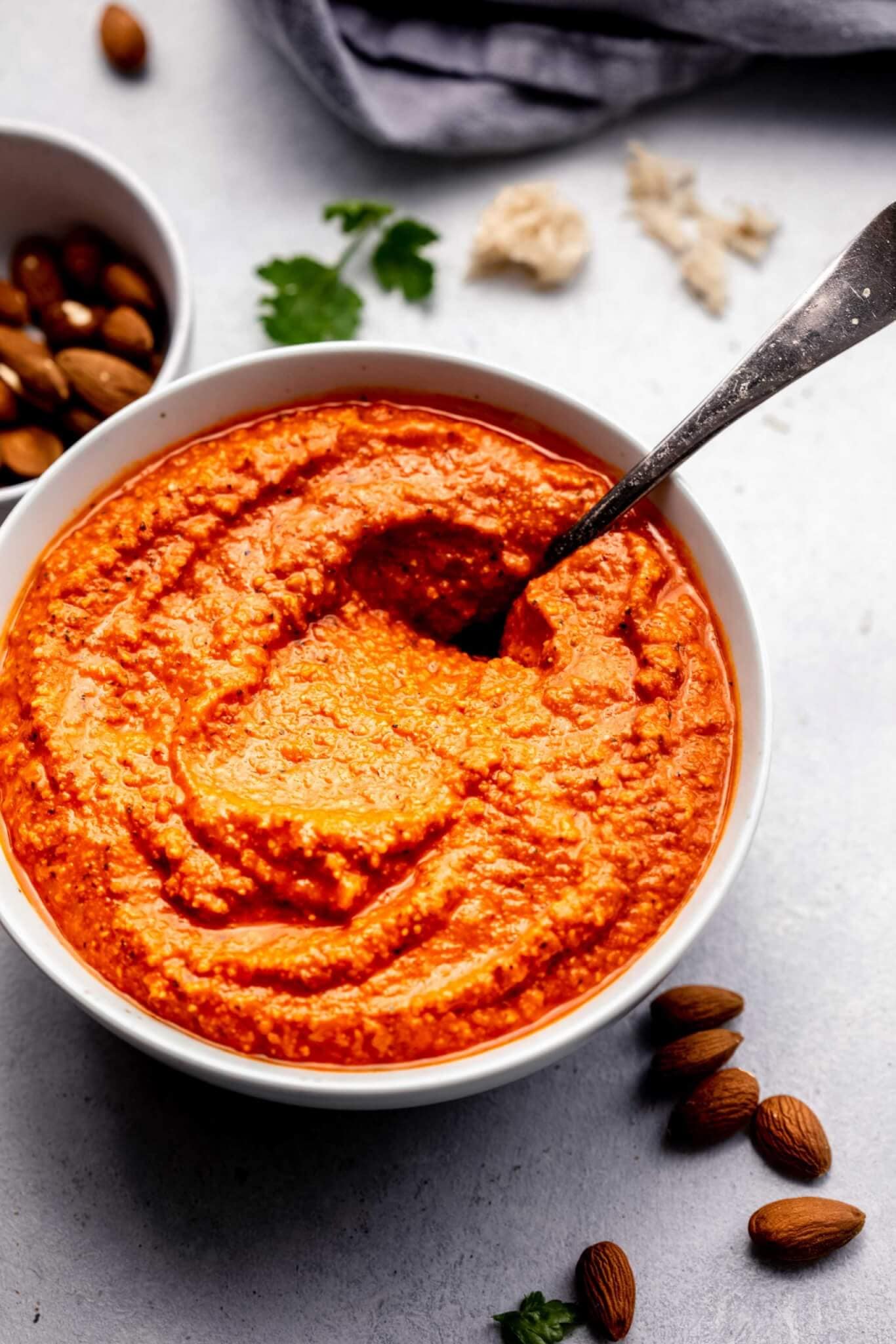 Romesco sauce in white bowl next to almonds and crusty bread.