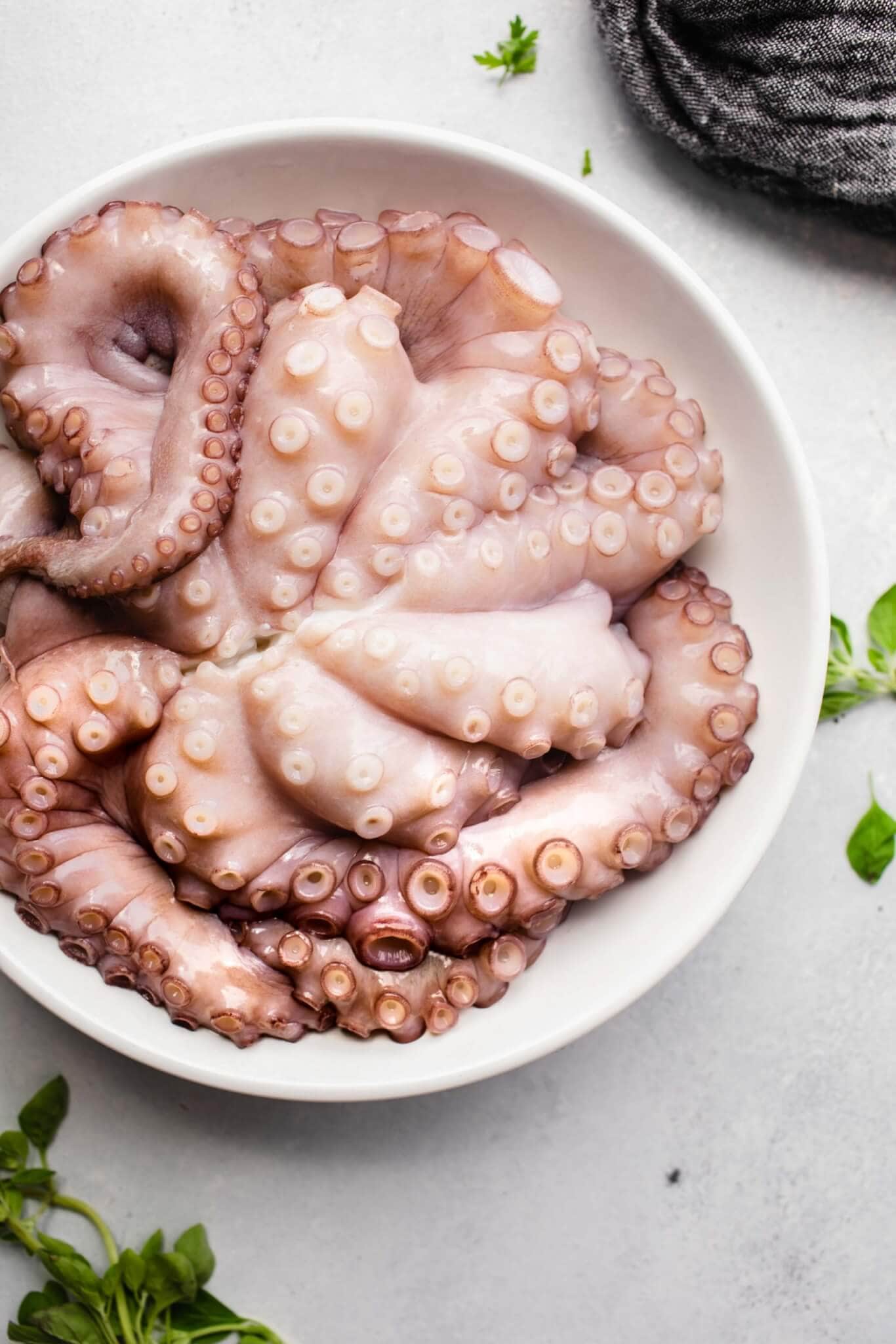 Uncooked octopus in large white bowl.