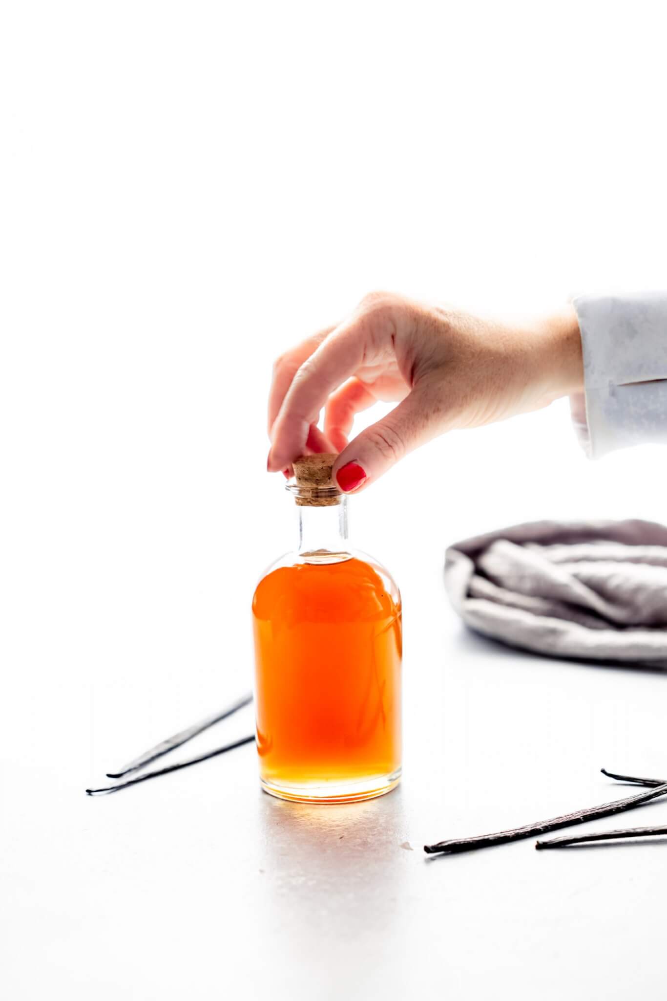 HAND PUTTING CORK ON BOTTLE OF VANILLA EXTRACT