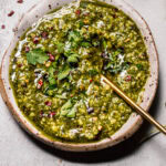 Overhead shot of chimichurri in small rustic bowl with gold spoon.