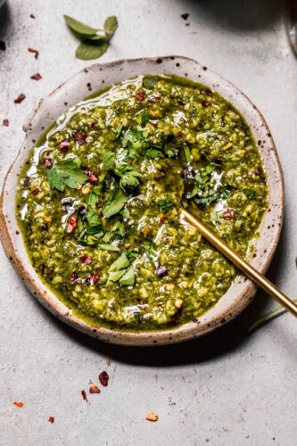 Overhead shot of chimichurri in small rustic bowl with gold spoon.