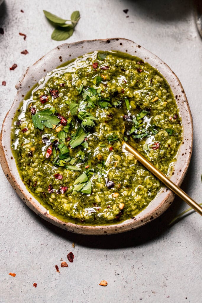 Overhead shot of chimichurri in small rustic bowl with gold spoon.