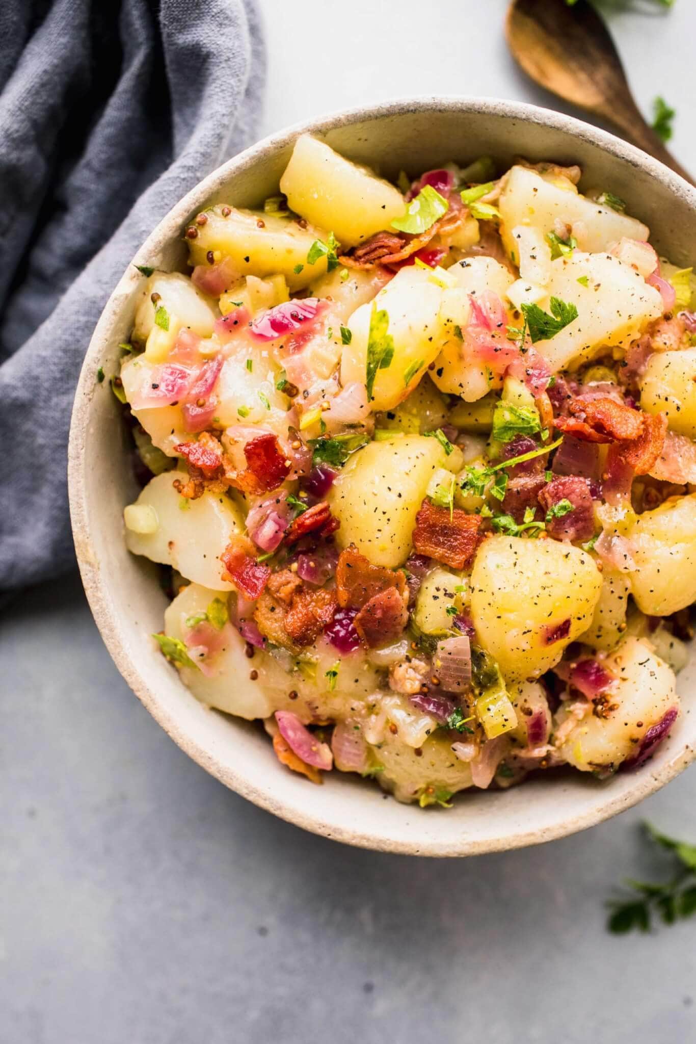 German potato salad in white bowl next to wooden spoon.