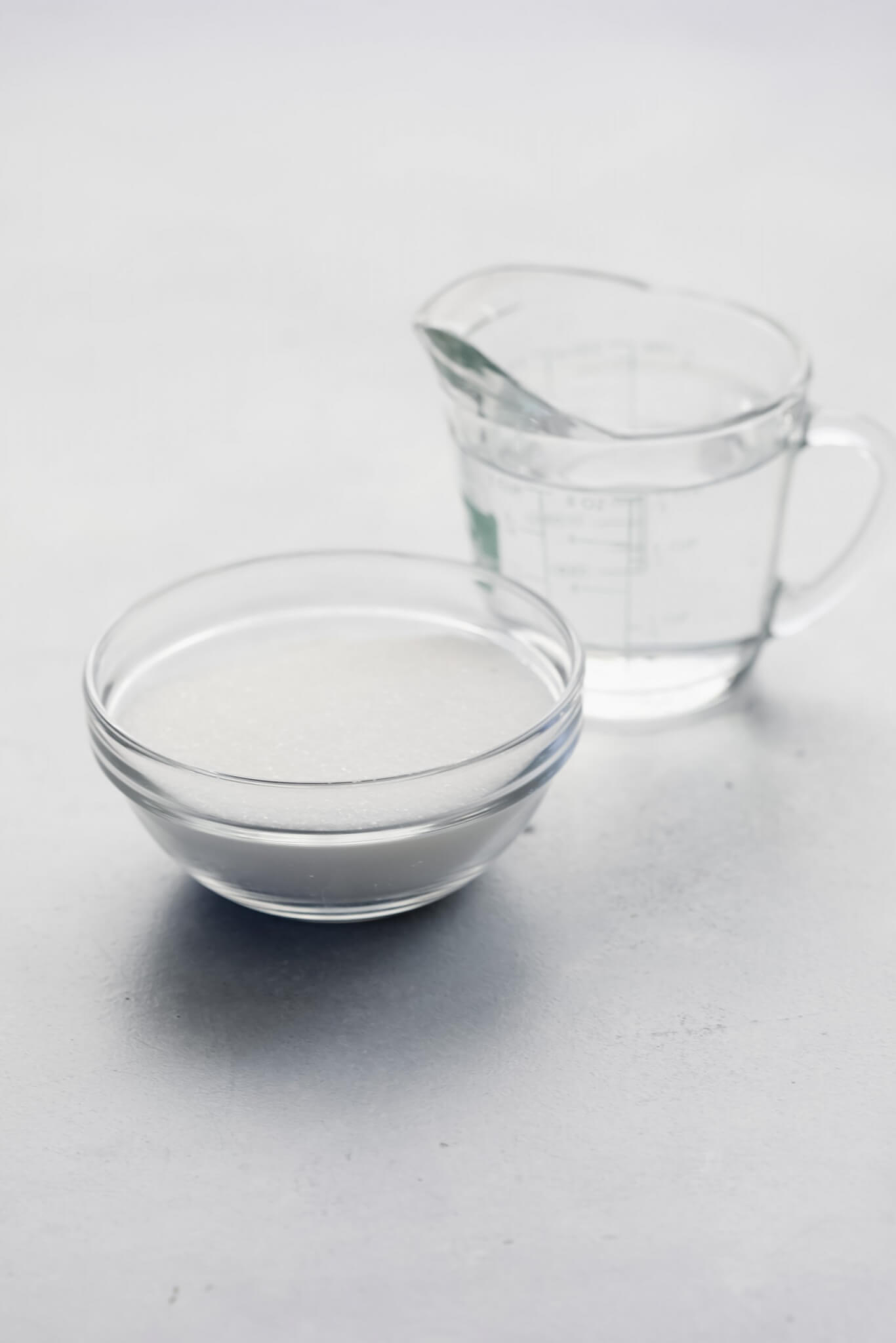 Bowl of sugar next to measuring cup filled with water. 