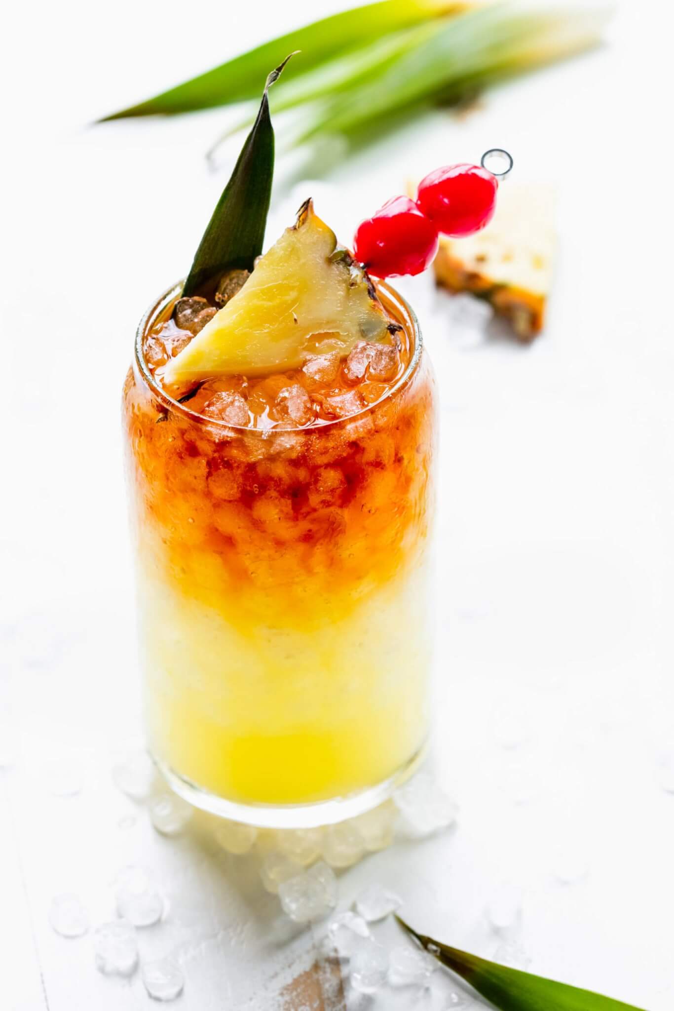 Mai tai cocktail in glass garnished with pineapple wedge and cherries.