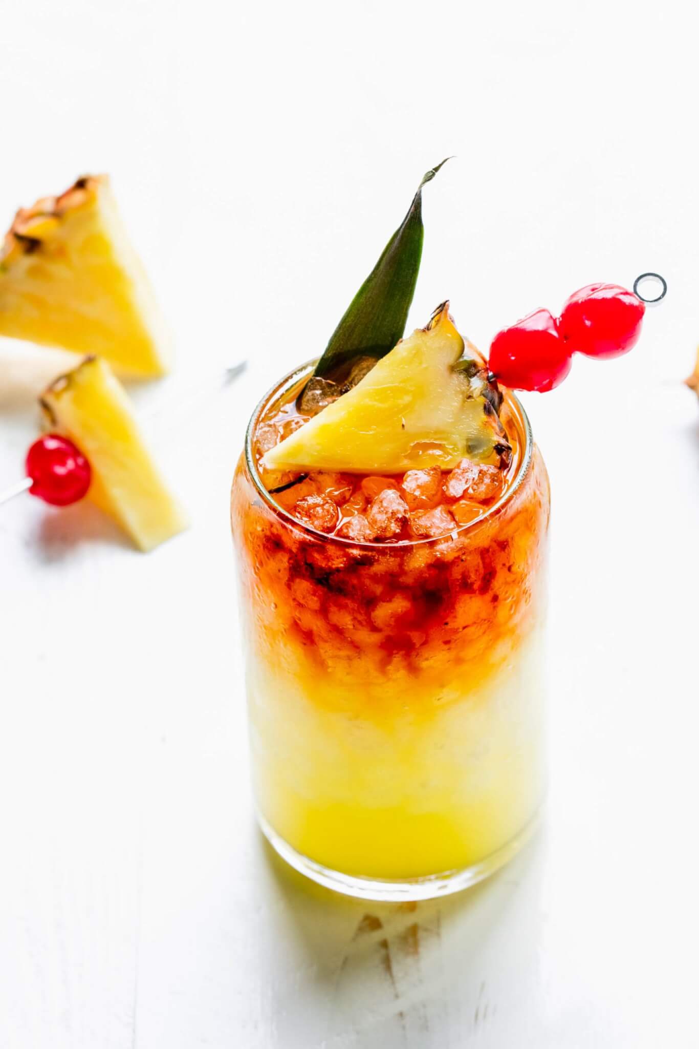 Mai tai in glass garnished with pineapple wedge and cherries.