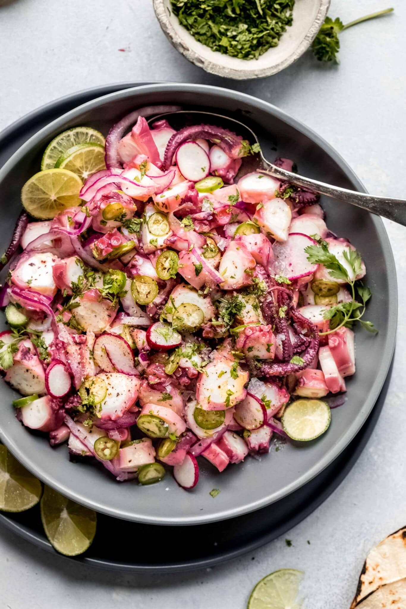 Overhead shot of octopus ceviche in large grey bowl next to lime slices and tortillas.