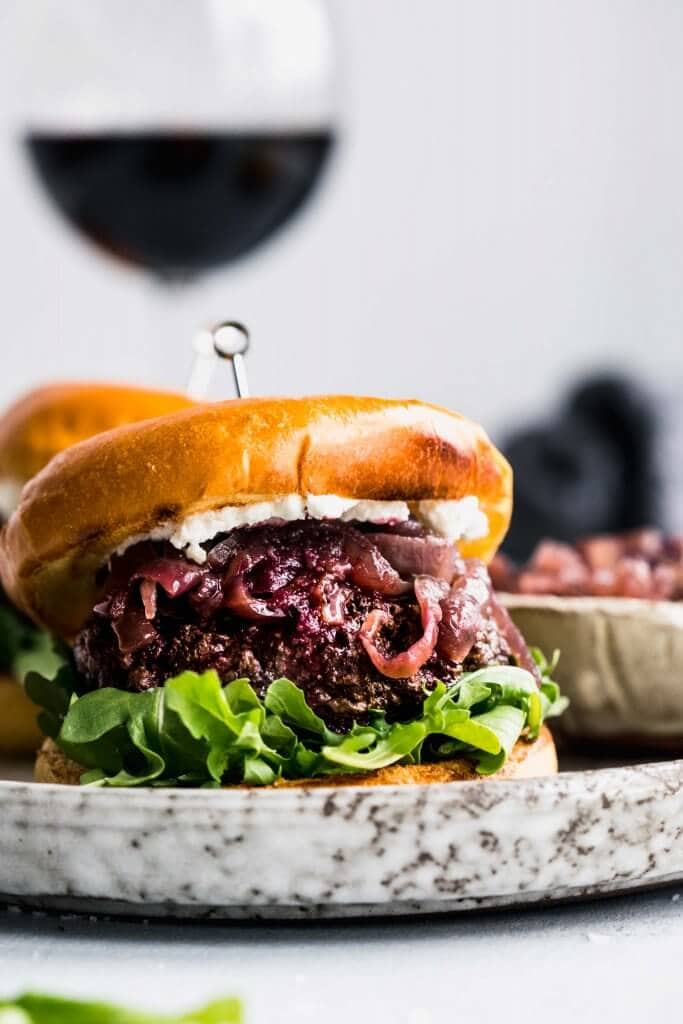 Side view close up of lamb burger on bun next to glass of red wine.