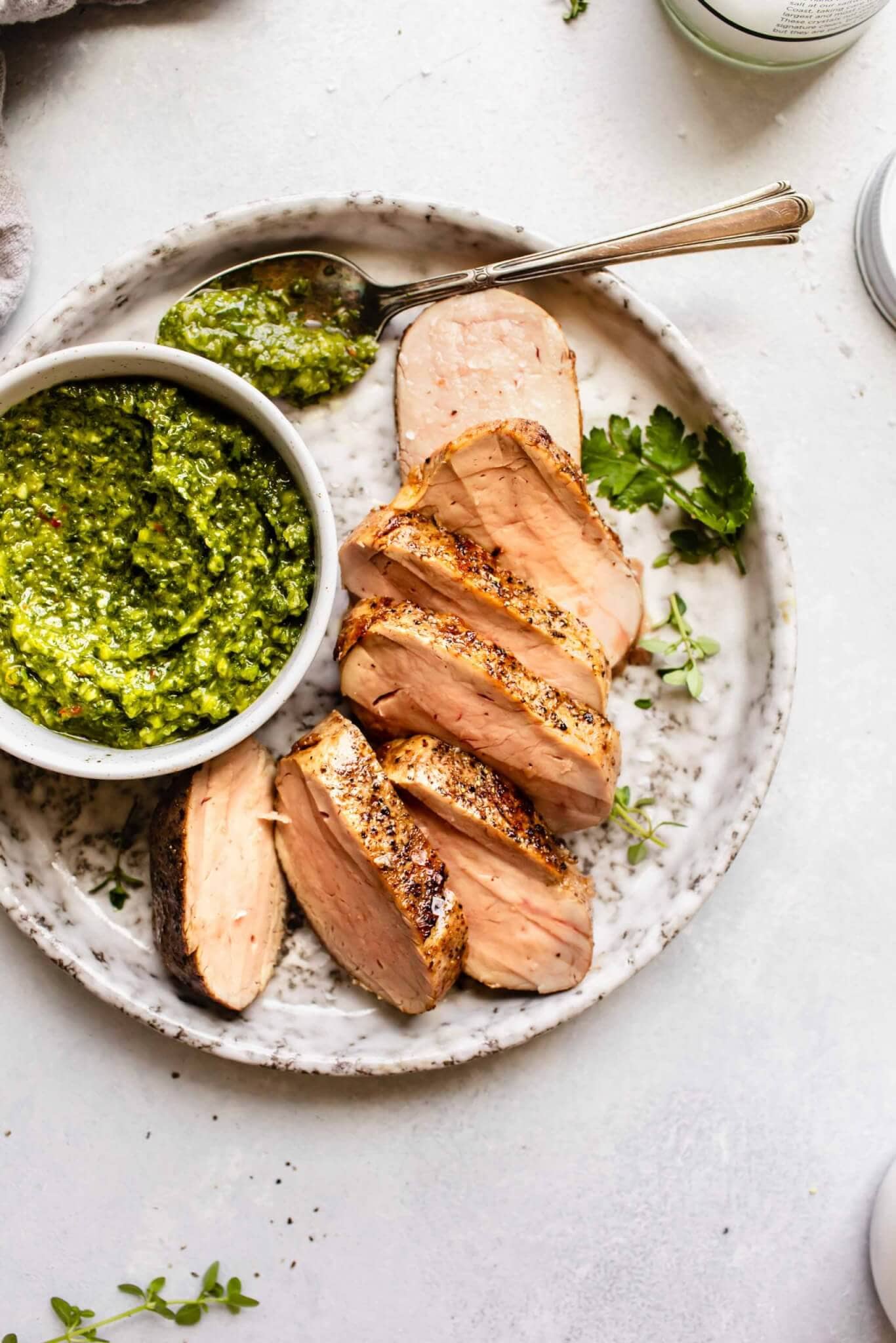 Overhead shot of sous vide cooked pork tenderloin on grey plate with bowl of chimichurri sauce.