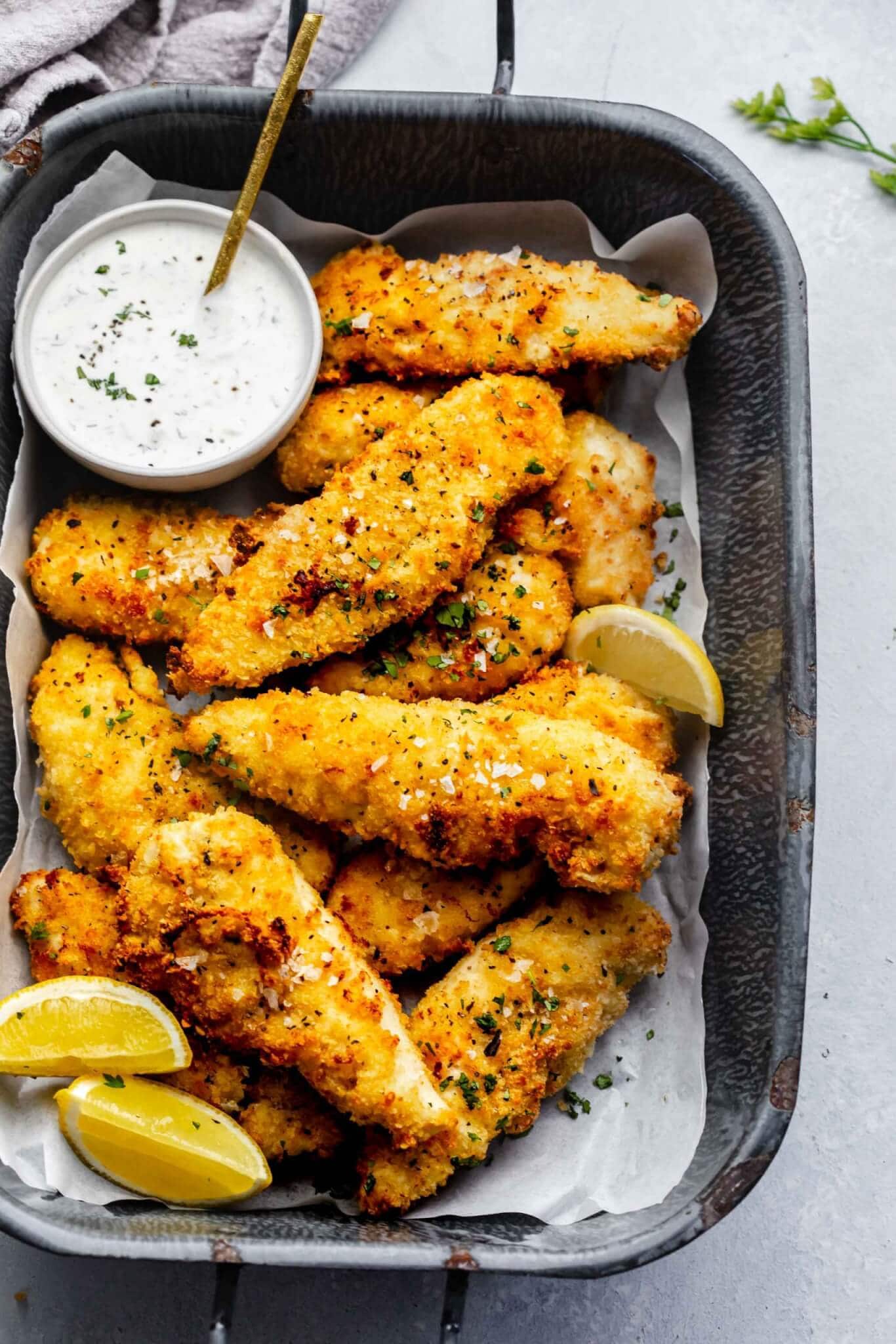 Air fried chicken tenders on serving tray with small bowl of ranch and lemon wedges.