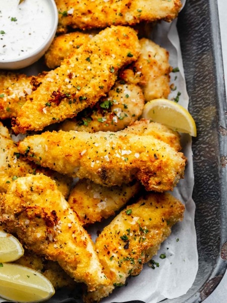 Air fried chicken tenders on serving tray with small bowl of ranch and lemon wedges.