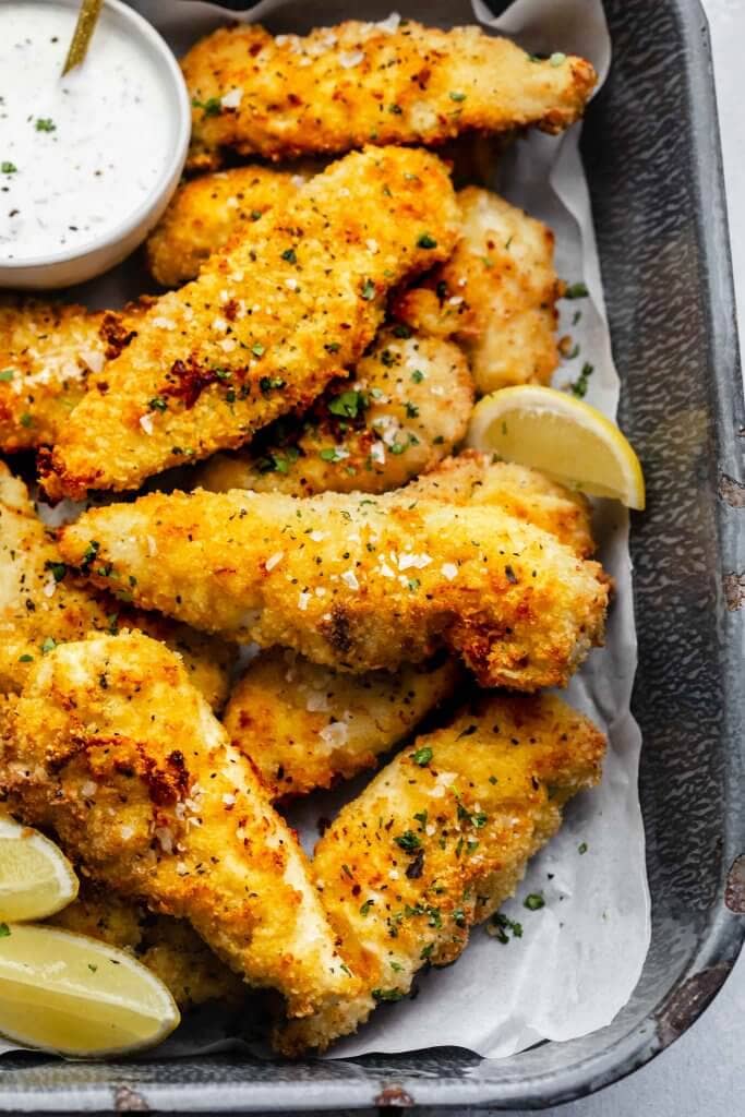 Air fried chicken tenders on serving tray with small bowl of ranch and lemon wedges.