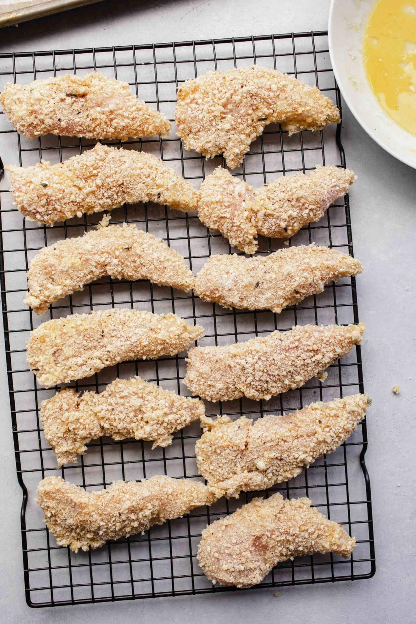 Breaded chicken strips on cookie rack before air frying.