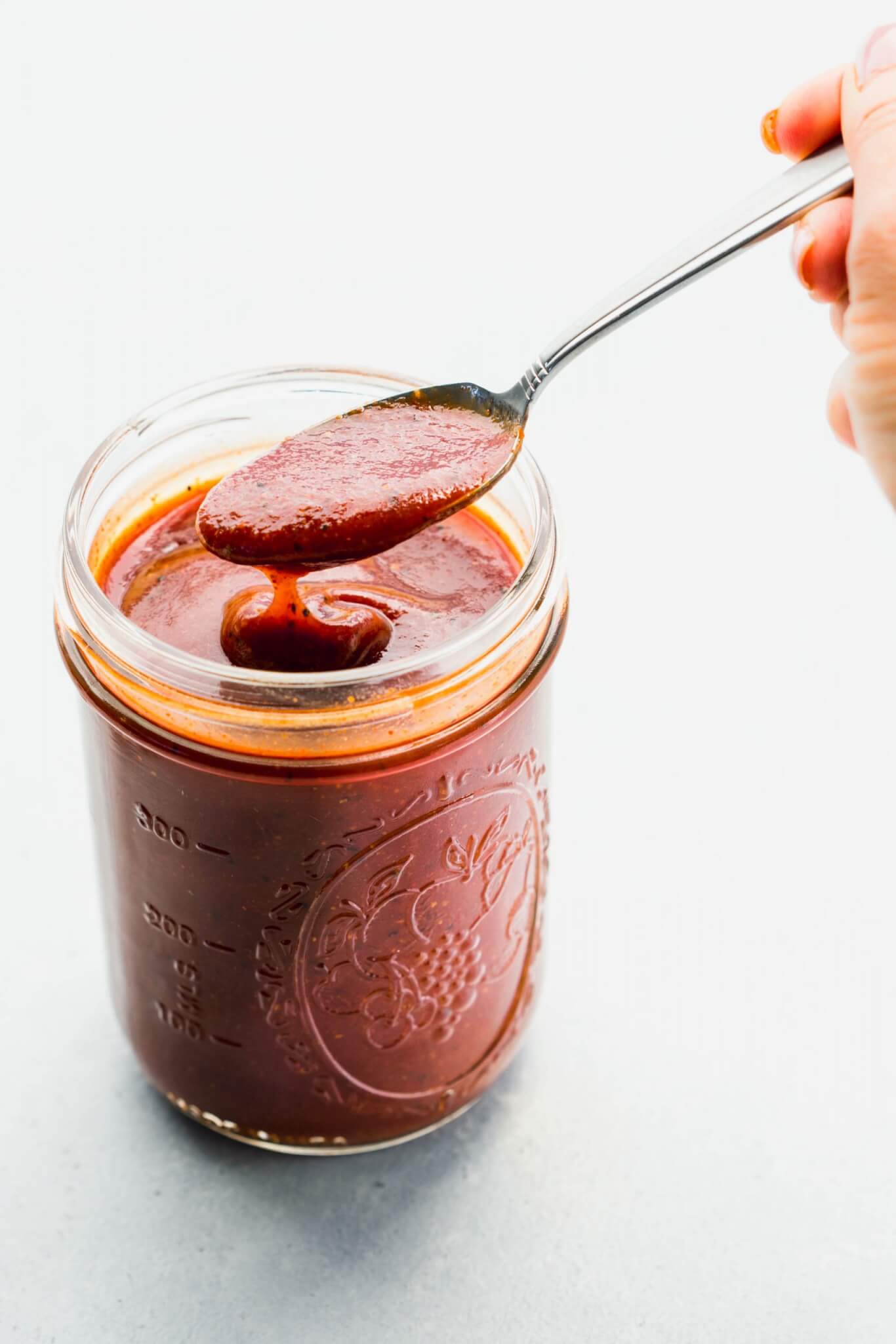 Spoon lifting bbq sauce out of jar.