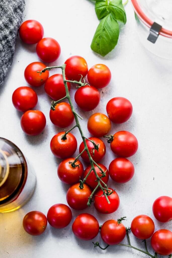 Stem of cherry tomatoes next to bottle of olive oil