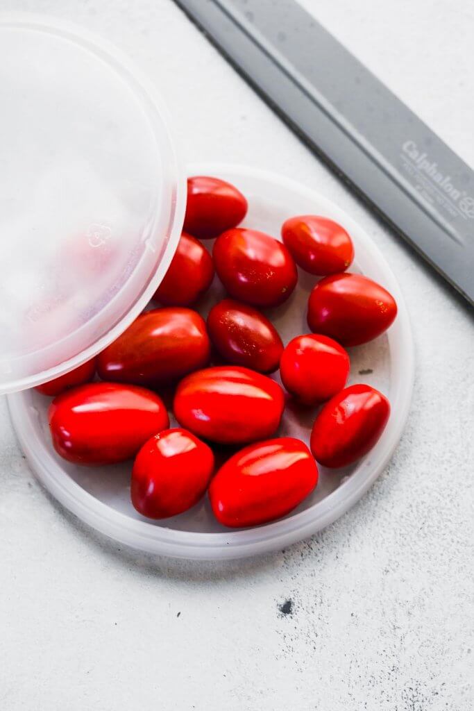 Cherry tomatoes sandwiched between two deli lids for slicing