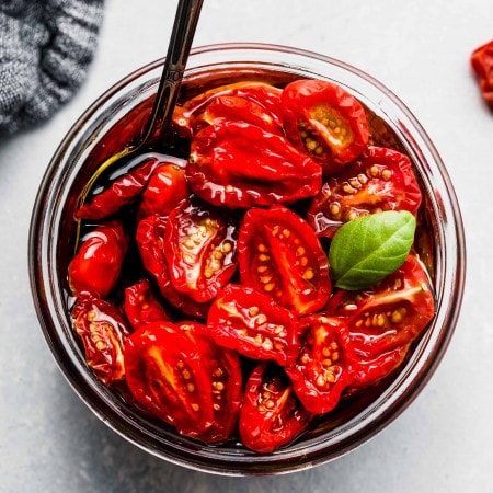 Overhead shot of sun dried tomatoes in small jar with a basil leaf.