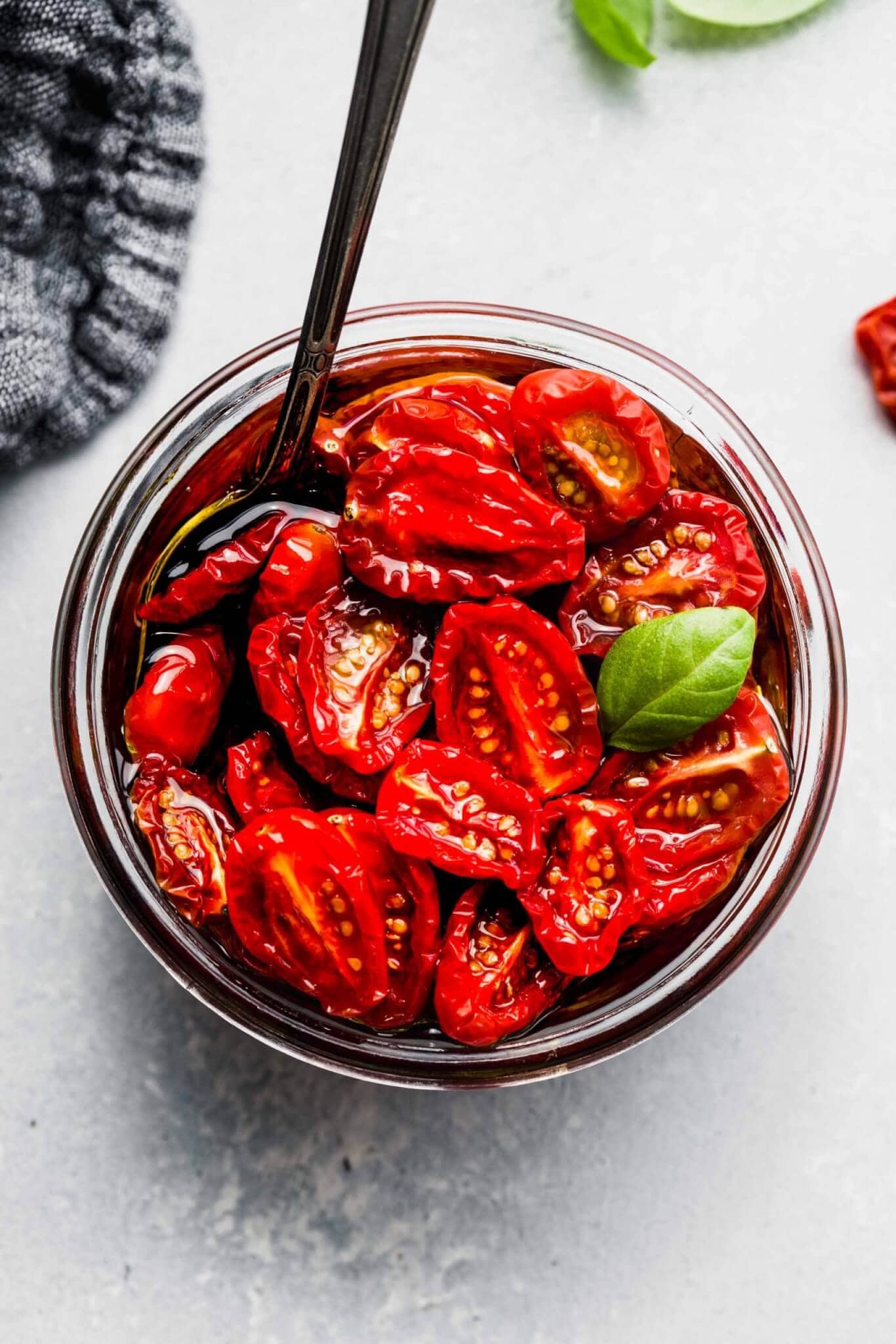 Overhead shot of sun dried tomatoes in small jar with a basil leaf.