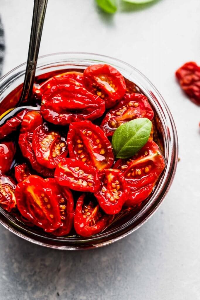 Jar of sun dried tomatoes with spoon and basil leaves. 