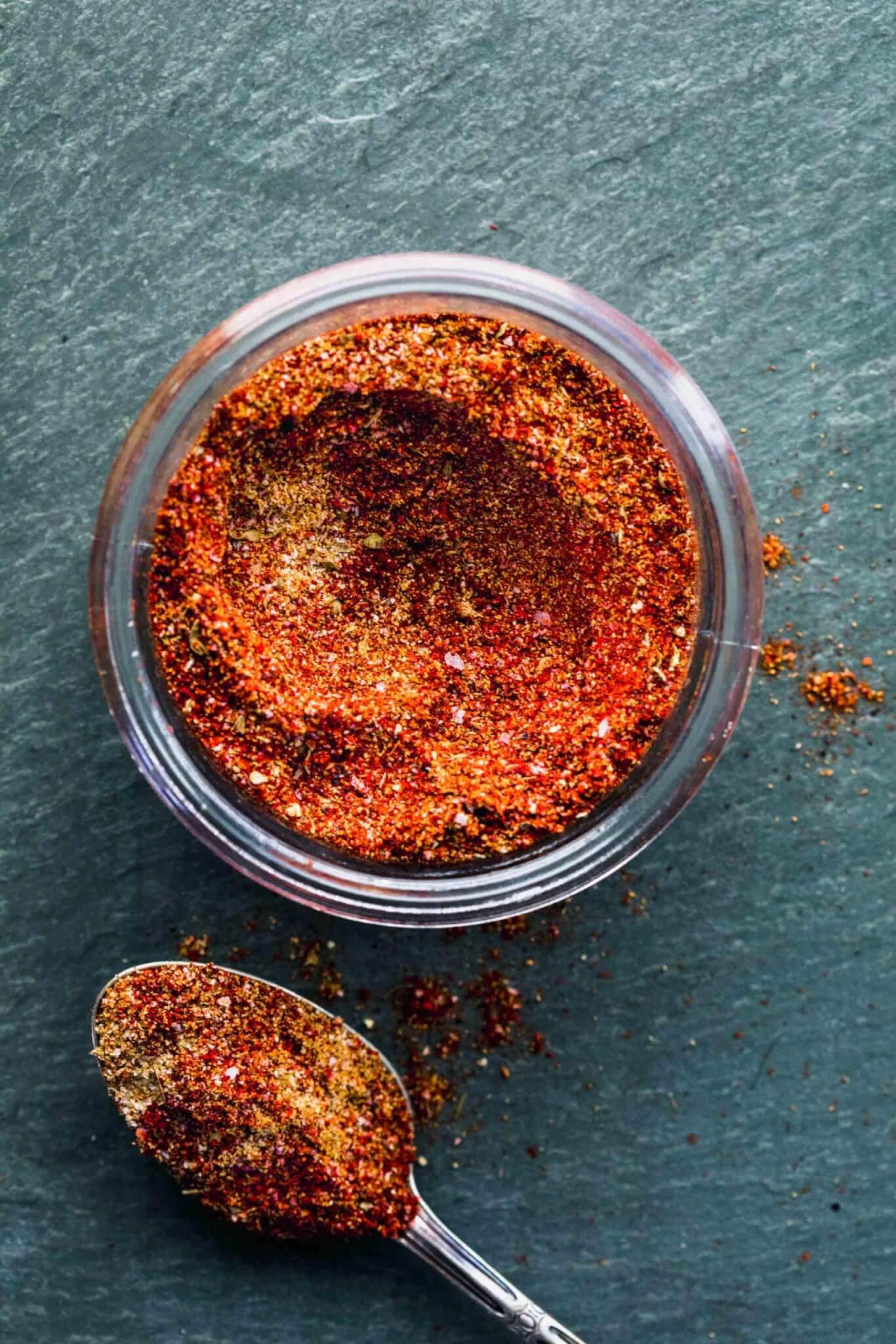 OVERHEAD SHOT OF TACO SEASONING IN GLASS CONTAINER WITH SPOON NEXT TO IT