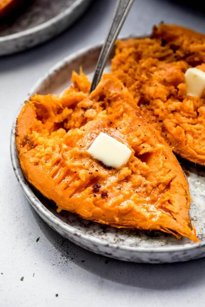 Split open sweet potato on grey plate with pats of butter and fork.