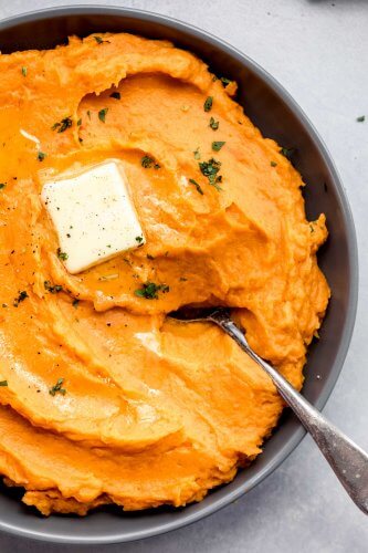 Overhead close up of bowl of mashed sweet potatoes with pat of butter.