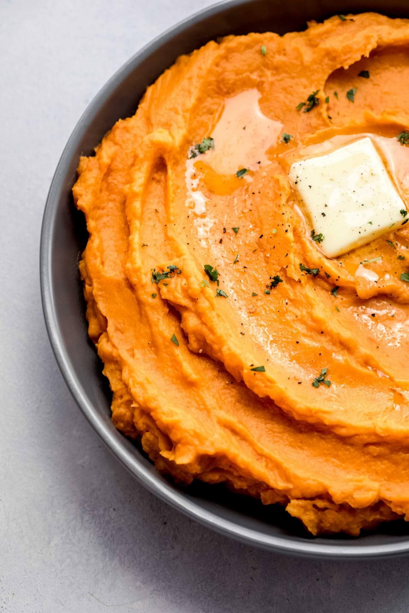 Overhead close up of bowl of mashed sweet potatoes with pat of butter. 