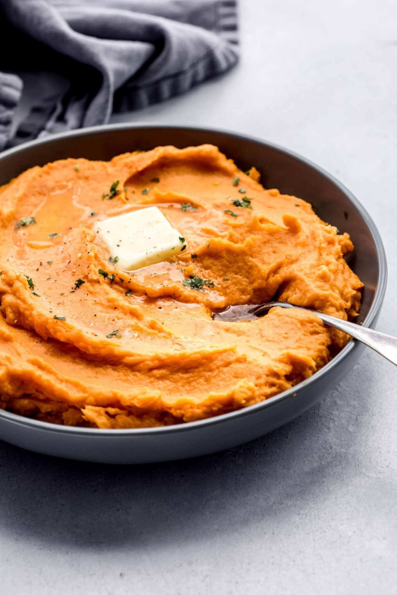 Side view of bowl of mashed sweet potatoes topped with pat of butter and chopped parsley.