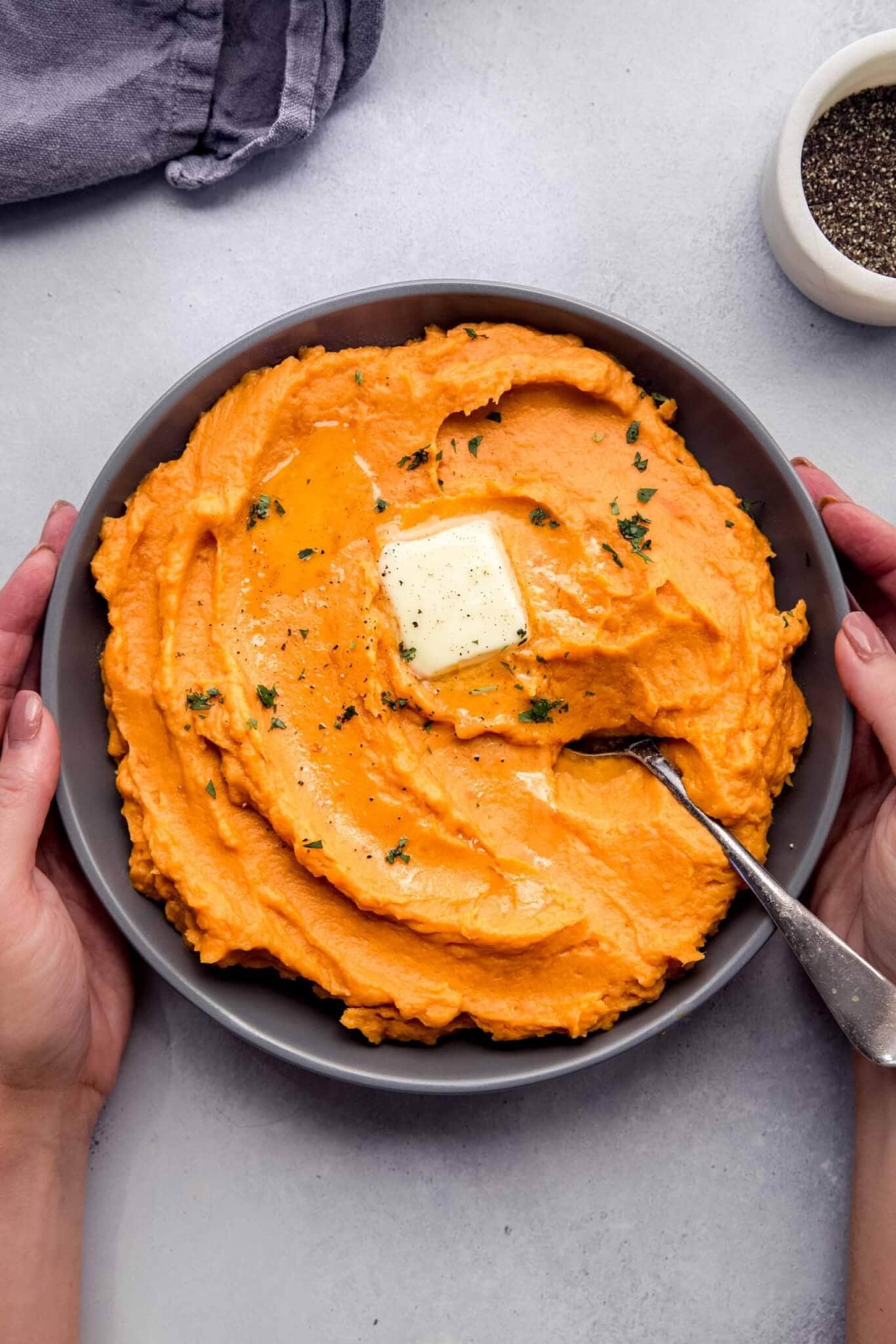 Hands holding bowl of mashed sweet potatoes.