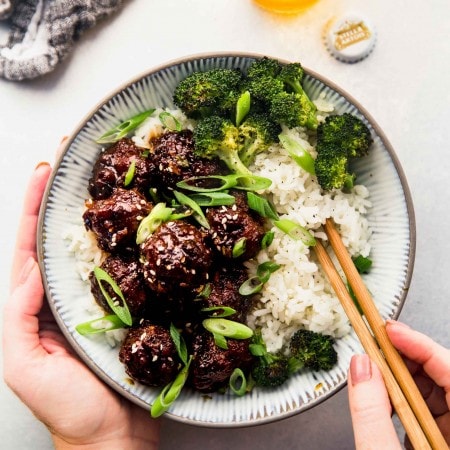Two hands holding bowl of mongolian beef meatballs and chopsticks