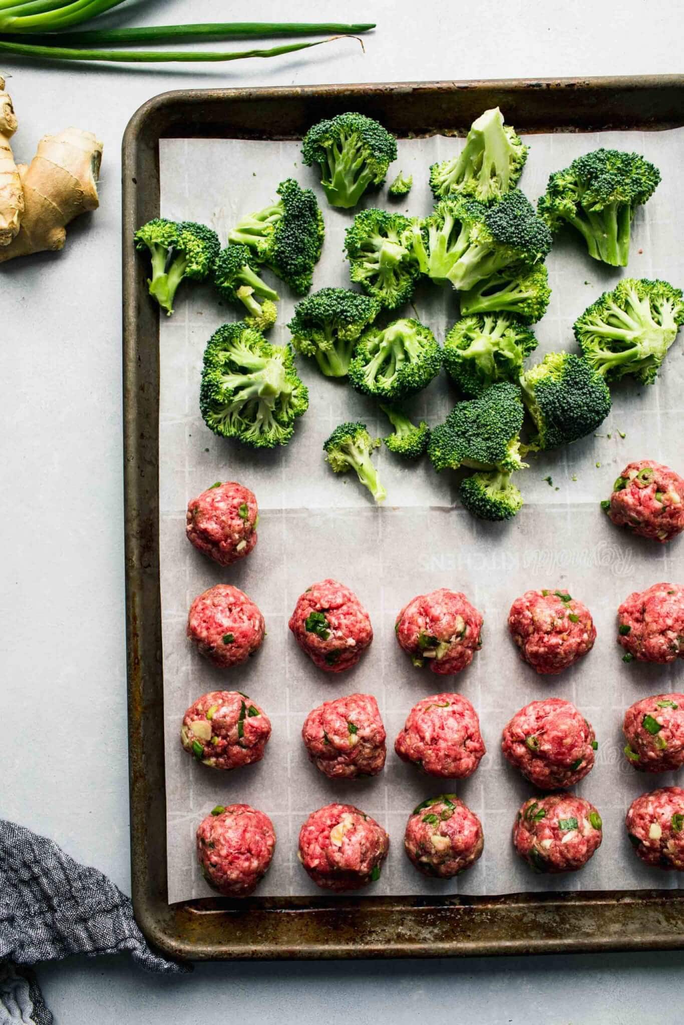 Uncooked meatballs and broccoli on baking sheet.