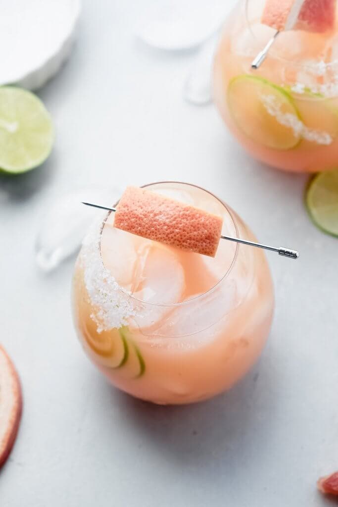 Side view of paloma cocktail garnished with grapefruit wedge. 
