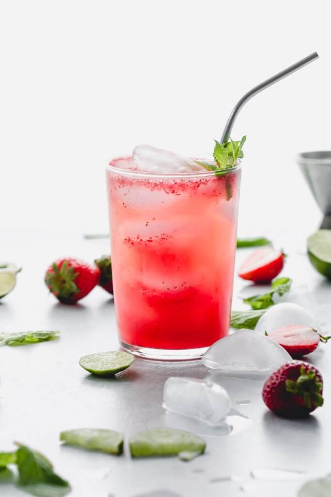 Side view of prepared strawberry mojito garnished with mint sprig and lime slices