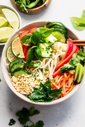 Vietnamese noodle salad in white bowl topped with chopped nuts and lime wedges.