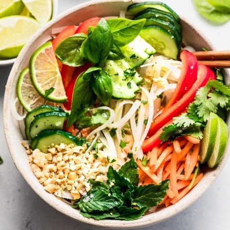 Vietnamese noodle salad in white bowl topped with chopped nuts and lime wedges.