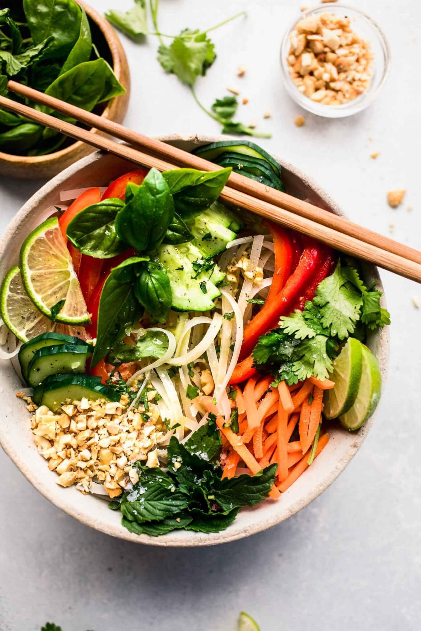 Vietnamese noodle salad in white bowl topped with chopped nuts and lime wedges.