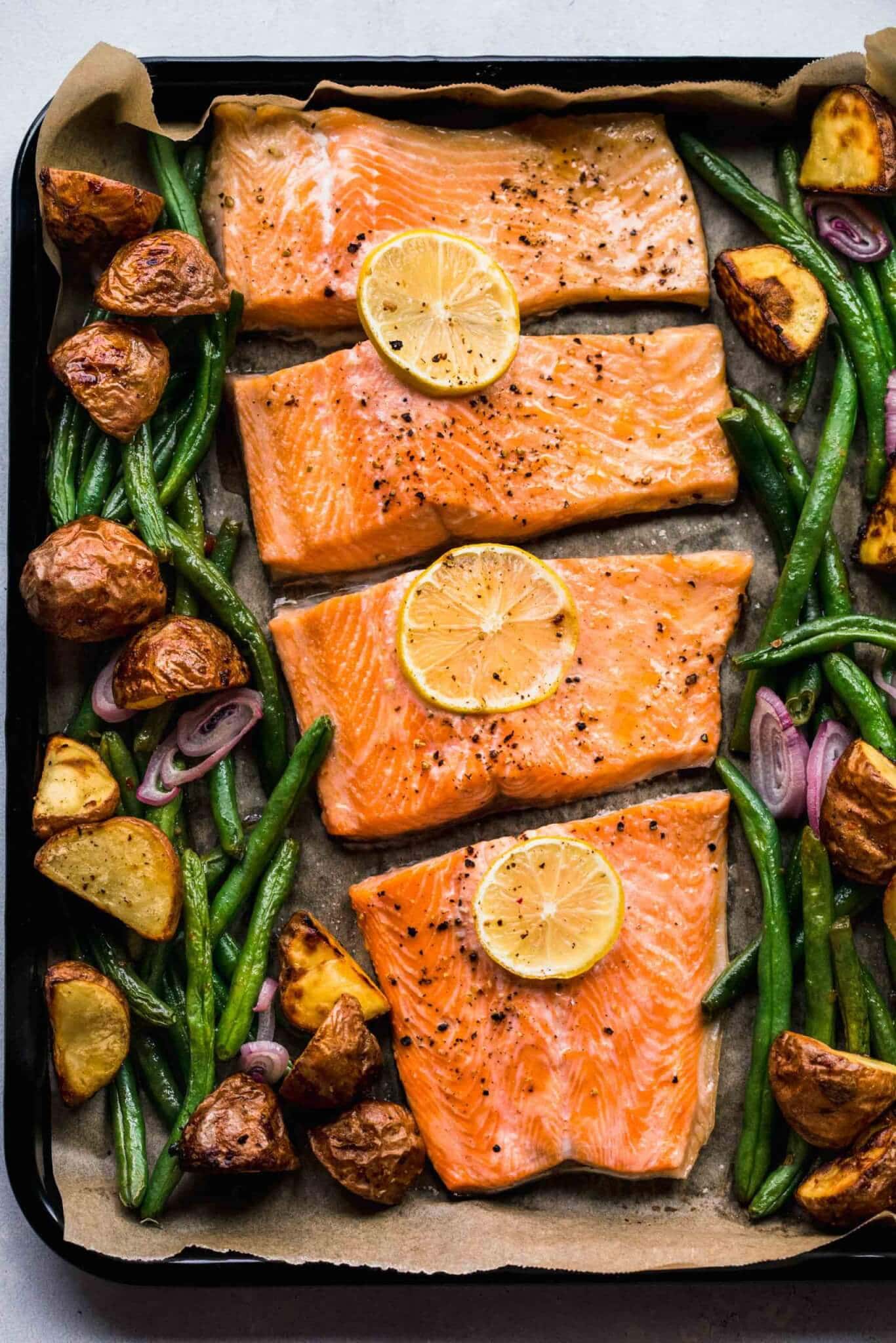 Salmon arranged on baking sheet with lemon slices.