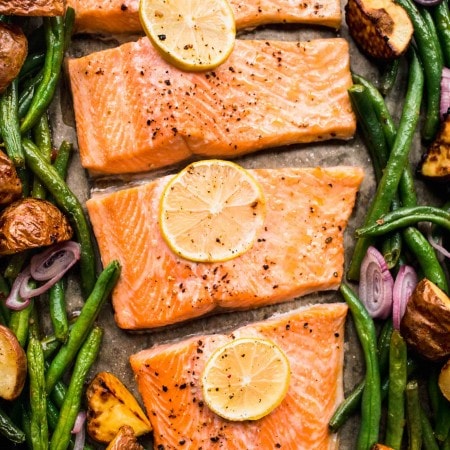 Salmon on baking sheet with green beans, potatoes and lemon slices.