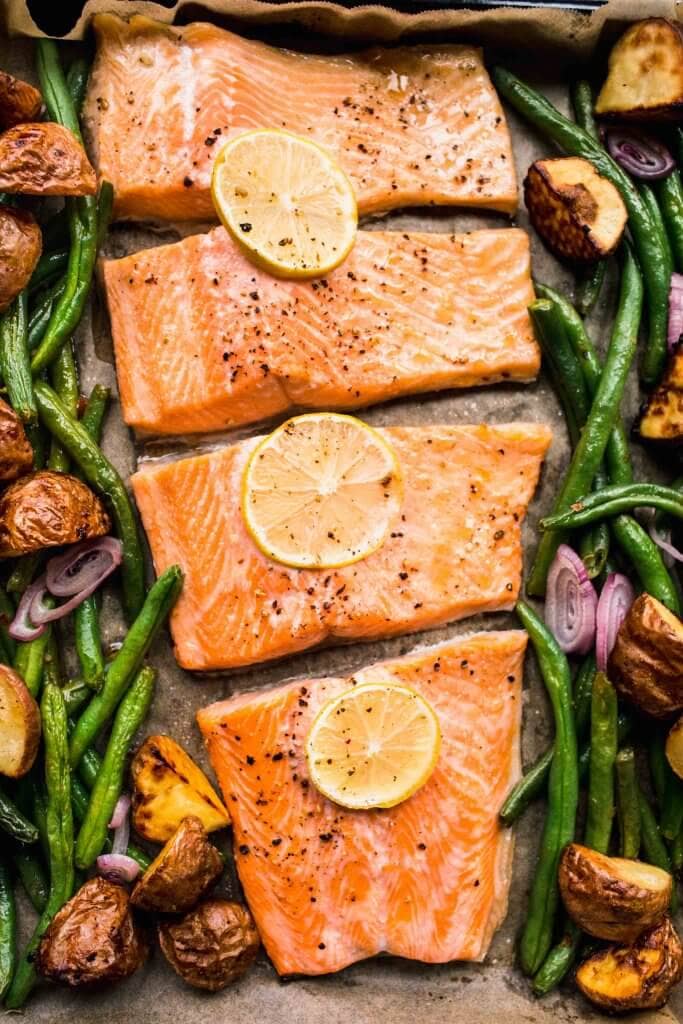 Salmon on baking sheet with green beans, potatoes and lemon slices.