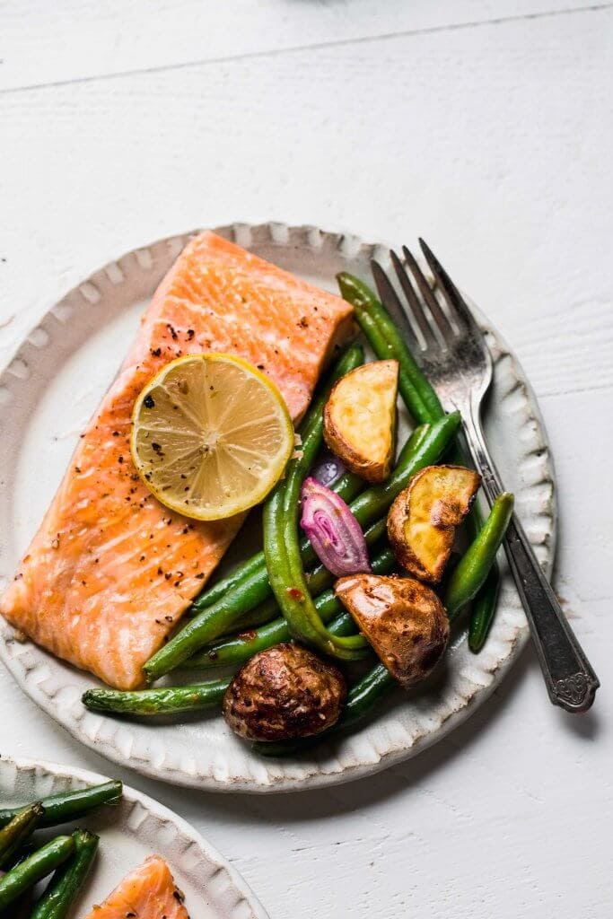Sheet pan salmon dinner served on small white plate. 