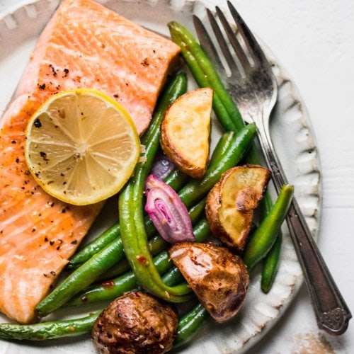 Baked salmon on plate with lemon slice, green beans and potatoes.