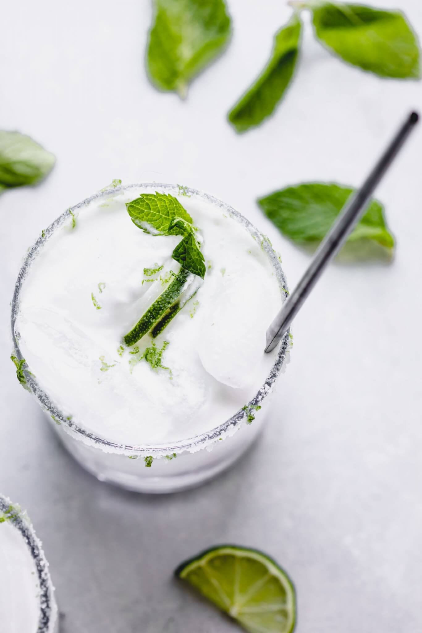 Overhead shot of coconut mojito in glass with lime slices and mint sprigs.