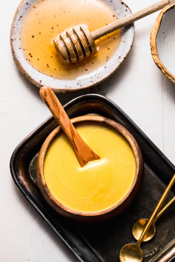 Overhead shot of honey mustard sauce in small wooden bowl with spoon next to bowl of honey.