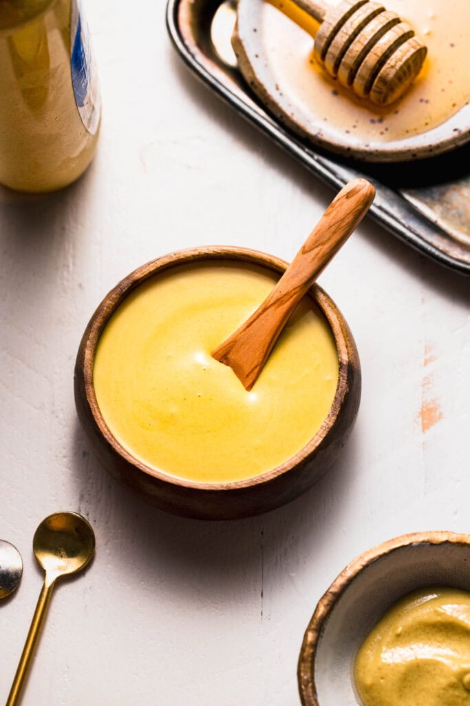 Small bowl of honey mustard sauce next to bottle of mustard.