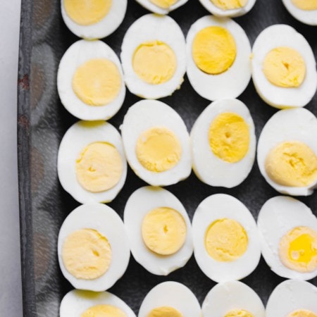 Hard boiled eggs sliced in half on grey tray.