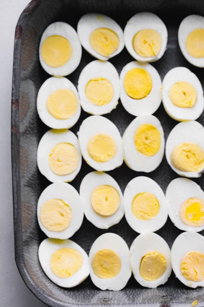 Hard boiled eggs sliced in half on grey tray.